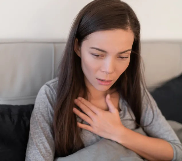 Frau hält sich die Hand an den Brustkorb, weil sie husten muss