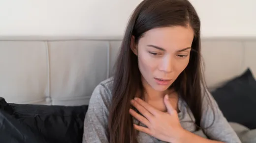 Frau hält sich die Hand an den Brustkorb, weil sie husten muss